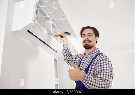 Happy AC repair service worker showing thumbs up while fixing wall air conditioner Stock Photo