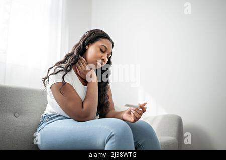 Unhappy black woman looking at pregnancy test upset by result sitting on couch Stock Photo