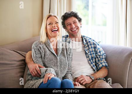 I can always make her laugh. Shot of a mature couple laughing while relaxing on their sofa at home. Stock Photo