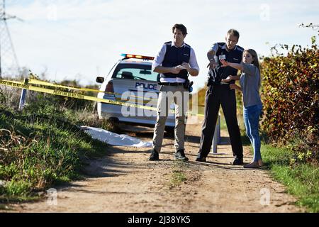 Getting her statement. Shot of a woman showing police officers where she found the body at a crimescene. Stock Photo