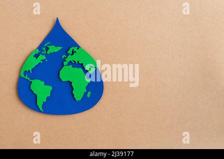 Water drop cut out on blue paper with world map on brown card stock background. Copy space. Stock Photo