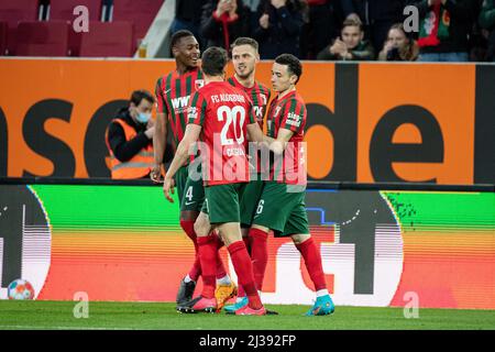 06 April 2022, Bavaria, Augsburg: Soccer: Bundesliga, FC Augsburg - FSV Mainz 05, Matchday 26, WWK Arena. Goal scorer Ruben Vargas of Augsburg (r) celebrates his team's goal to make it 2:1. Reece Oxford (l-r), Daniel Caligiuri and Jeffrey Gouweleeuw of Augsburg stand around him. Photo: Matthias Balk/dpa - IMPORTANT NOTE: In accordance with the requirements of the DFL Deutsche Fußball Liga and the DFB Deutscher Fußball-Bund, it is prohibited to use or have used photographs taken in the stadium and/or of the match in the form of sequence pictures and/or video-like photo series. Stock Photo