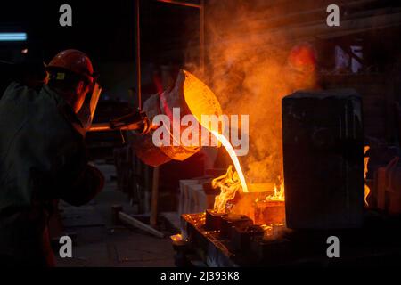 Two workers filling out mold with molten metal in factory. Stock Photo