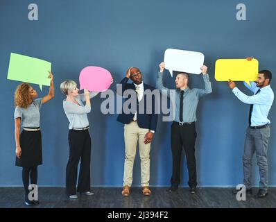 What did I get myself in to. Shot of a man looking overwhelmed as people hold up speech bubbles around him. Stock Photo