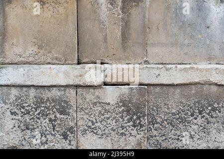 Big old stone blocks as part of a solid wall. Building exterior background of a vintage house. Grey weathered rough textures with dirt spots. Stock Photo