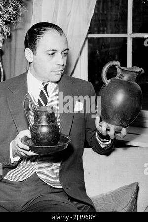 Actor Adds B.C. Pottery To His Collection - Actor Herbert Lom seen in his Kensington (London) flat proudly looking at the pieces of Etruscan pottery which he recently acquired while filming in Rome. On the left is a drinking mug and platter (4th. Century B.C.) and on the right the jug (5th. Century B.C.). Actor Herbert Lom collects antiques as a hobby and whilst filming in Italy recently for Tolstoy's 'War and Peace', in which he plays the part of Napoleon, he made some very valuable additions to his growing collection. November 25, 1955. (Photo by Fox Photos). Stock Photo