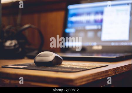 A selective focus of a wireless mouse on the wooden table with a laptop and headphones on background Stock Photo