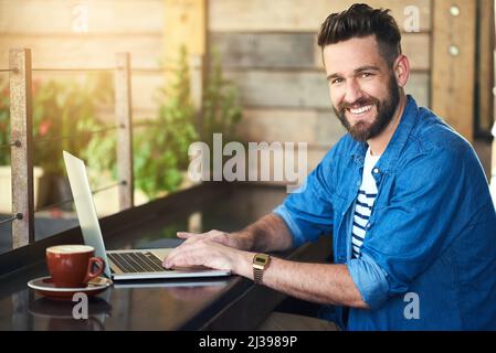 I come here for the benefit of free wifi. Portrait of a handsome young man working on his laptop in a cafe. Stock Photo