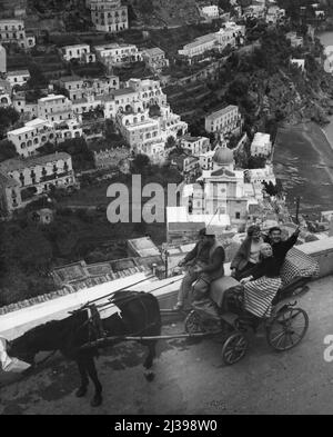 Haven For Artists -- This view shows how Positano lies along the small beach and against the jagged rooks. Riding in a colorful horse-drawn carriage, writer Reynolads Packard, of the New York daily news, points out some of the more interesting rock formations to painting students Jonna Brasoh, 23, from Denmark, and Carine Knief, 20, from Germany (Foreground). December 03, 1954. (Photo by United Press). Stock Photo