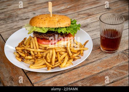 Hamburger and fries. Tasty burger with cheese, lettuce, beef and tomatoes served outdoor on a wooden table with a glass of coca. Stock Photo