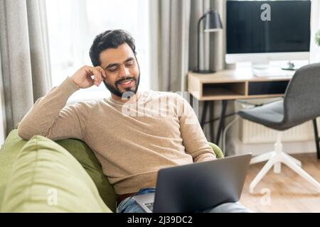 Diverse office employee concept. Focused indian man using laptop for online video conversation, talking with customers or coworkers online while sitting at the sofa Stock Photo