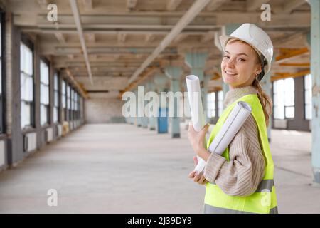 Woman architect in protective helmet and yellow vest checks building renovation project on drawings Stock Photo