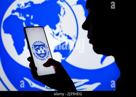 In this photo illustration, a woman's silhouette holds a smartphone with the International Monetary Fund (IMF) logo displayed on the screen and in the background. Stock Photo