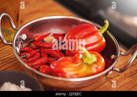 Some like it hot. Shot of a pan filled with red peppers and chillies on a tabletop. Stock Photo