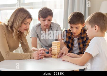 A family, three boys and a woman, are enthusiastically playing a board game Stock Photo