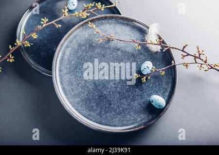 Easter dish decorated with blue eggs, feathers and spring branches. Ceramic plate on grey background. Space. Holiday mockup Stock Photo
