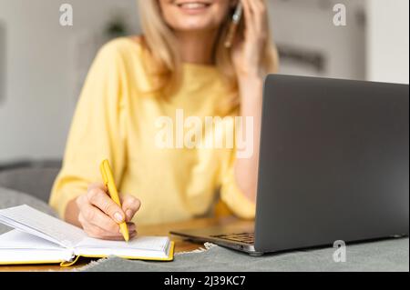 Cropped view of the senior bossy businesswoman having phone conversation working with a laptop at the desk in office. Aged saleswoman talking with a customers by smartphone Stock Photo