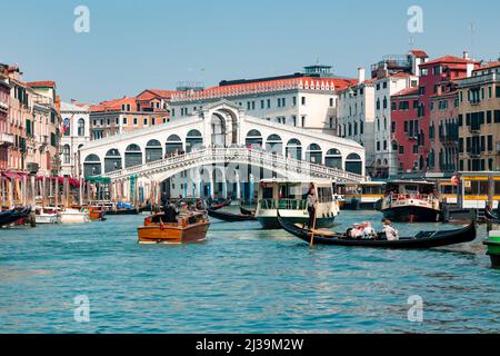 VENICE, ITALY - MARCH 27 2022: Crowds of tourists and boats at the famous Rialto Bridge spanning the Grand Canal of the city of Venice Stock Photo