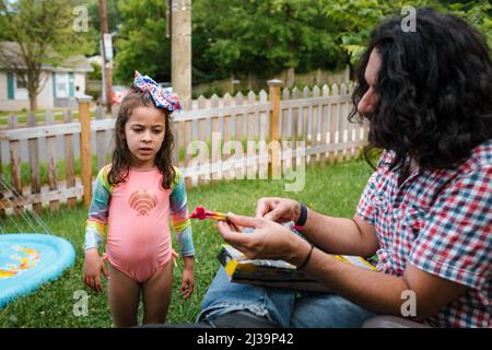 Father lighting sparkler for daughter on fourth of July Stock Photo