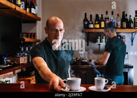 Two waiters at work, preparing coffee for their customers. Two co-workers in their small business. Stock Photo