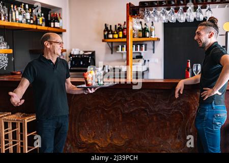 Co-workers serving drinks to their customers. Co-workers talking in their small business. Stock Photo