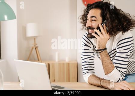 Cheerful man talking on phone with his laptop next to him at home Stock Photo