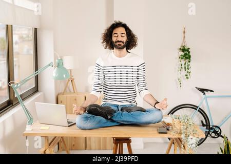 Young man meditating on desk at home Stock Photo