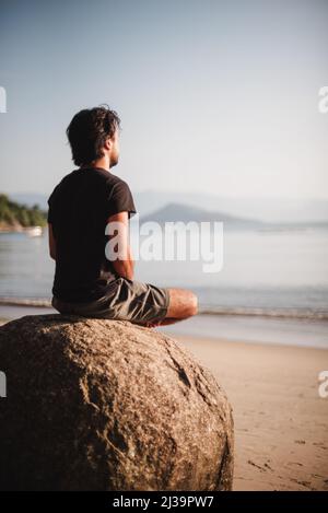 Man siting on a rock meditating on the beach Stock Photo