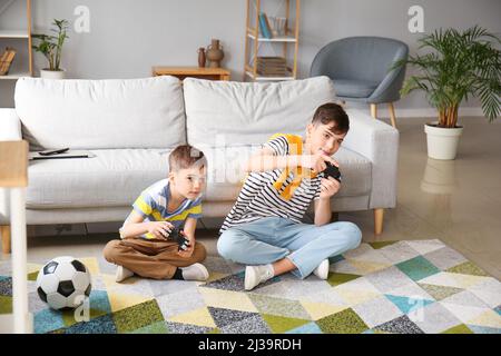 Two brothers playing football video game console, sitting on yellow pouf in  kids play center Stock Photo - Alamy