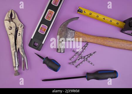 Flatlay of Hand Tools Pruple Background Including Hammer, Nails, Tape Measure, Level, Screwdrivers Stock Photo