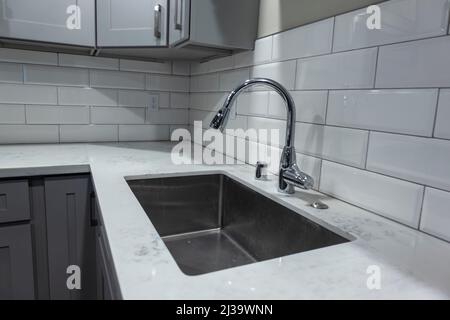 Angled view of a white, empty kitchen with marble countertops and a gas stove, the faucet in view in the background Stock Photo