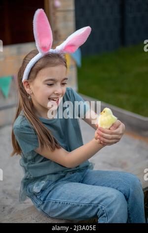 a cute girl in bunny ears is holding a chicken. Happy easter. Stock Photo