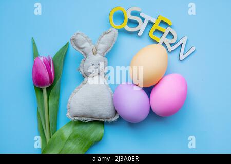 easter bunny, tulip, easter eggs and the inscription easter in german on a blue background. simple minimalism flat lay top view copy space, Happy East Stock Photo