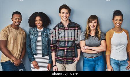 Good friends stand together. Studio portrait of a diverse group of young people standing together against a gray background. Stock Photo