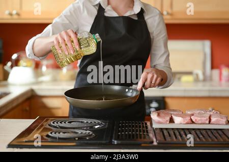The chef prepares fresh pork steaks in the kitchen, pours butter on the meat of the menu, cooking home cooking. culinary recipes. restaurant menu. Stock Photo