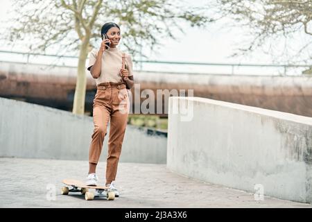 There are no shortcuts to any place worth going. Shot of an attractive young female student using her mobile phone while skateboarding on campus. Stock Photo