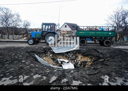 Kyiv, Ukraine. 06th Apr, 2022. A tractor drives past a crater in Demydiv, Ukraine following the Russian occupation of the small village. With the withdrawal of Russian troops from the villages surrounding Kyiv, Ukraine's Capitol, civilians who left are returning home to scenes of destruction and a lack of heat, water, and electricity. Credit: SOPA Images Limited/Alamy Live News Stock Photo