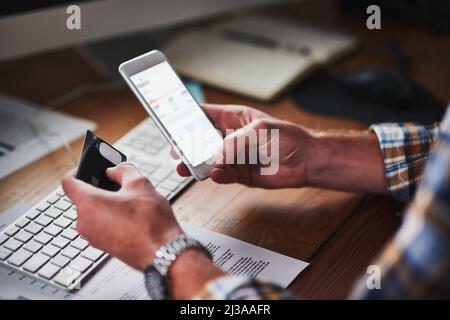 You dont need to leave your desk to shop. Shot of an unidentifiable programmer holding his credit card while using his smartphone. Stock Photo