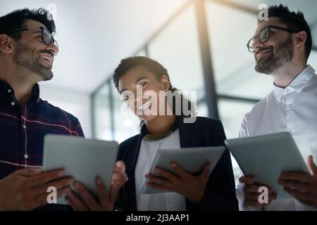 Tech savvy professionals at work. Shot of three colleagues using digital tablets while standing together in an office. Stock Photo
