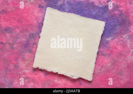 small square sheet of blank white Khadi paper against purple and pink marbled paper Stock Photo