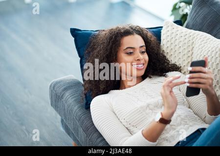 Connecting with old and new friends. Shot of a young woman using her cellphone while relaxing at home. Stock Photo