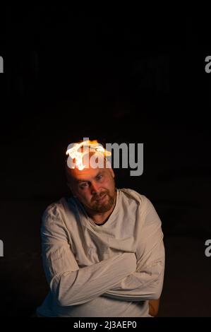 Bald man in a straitjacket with a burning head on a dark background. Stock Photo