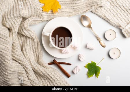 Autumn composition. Hot chocolate, warm wool sweater and autumn leaves, marshmallows and candles on a white background. flat lay, top view. Stock Photo