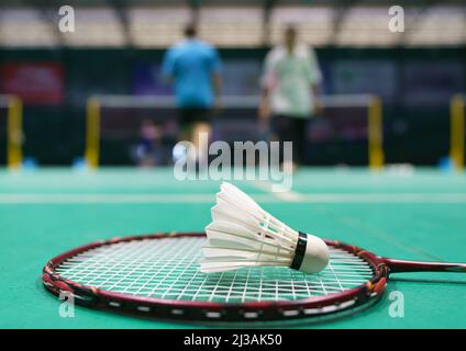 shuttlecock on green badminton playing court with player in background Stock Photo