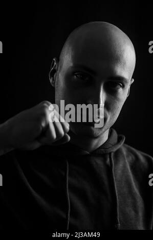 Black and white portrait of a young bald man showing his fist in defiance Stock Photo