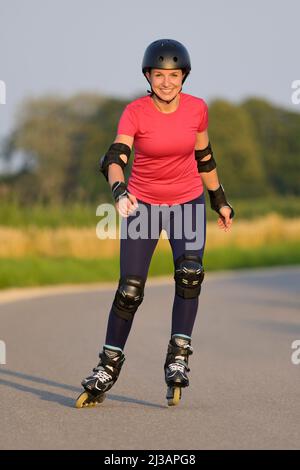 Young woman wearing protectors and helmet rollerblading on a small road. Stock Photo