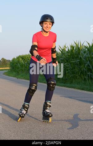 Young woman wearing protectors and helmet rollerblading on a small road. Stock Photo