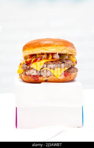 Double decker donut bun burger with beef patties and dressing on top of a takeaway box. Stock Photo