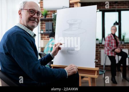 Portrait of elder student using pencil to draw vase sketch on canvas in ...