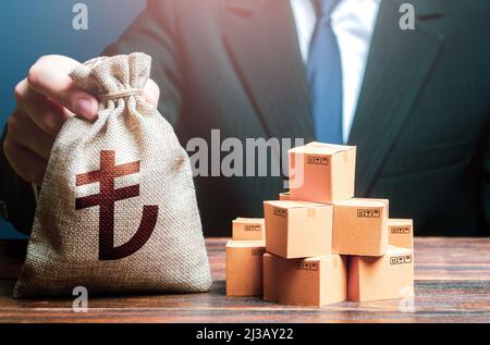 Businessman holds turkish lira money bag and boxes with goods. Business income. Payment of taxes and fees. Advertising budget. Purchase and sale of go Stock Photo